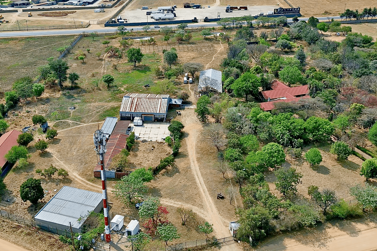 Aerial view of a large plot featuring multiple outbuildings, a telecommunications tower, mature trees, and extensive unpaved grounds.