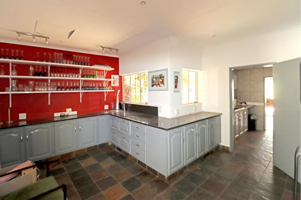 Kitchen featuring grey cabinetry, granite countertops, slate tile flooring, and open shelving against a red accent wall, with an adjacent scullery area.