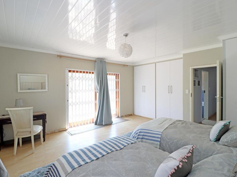 Spacious bedroom featuring built-in cupboards, laminate flooring, and a sliding glass door with security gate providing access to the exterior.