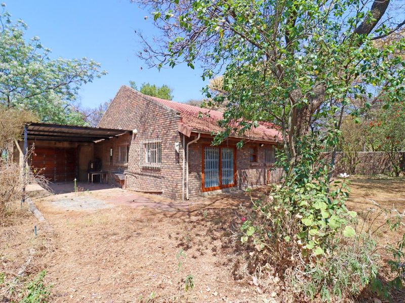 Rear view of a face brick house featuring a carport, sliding doors with security bars, and an external sink, set within a large garden.