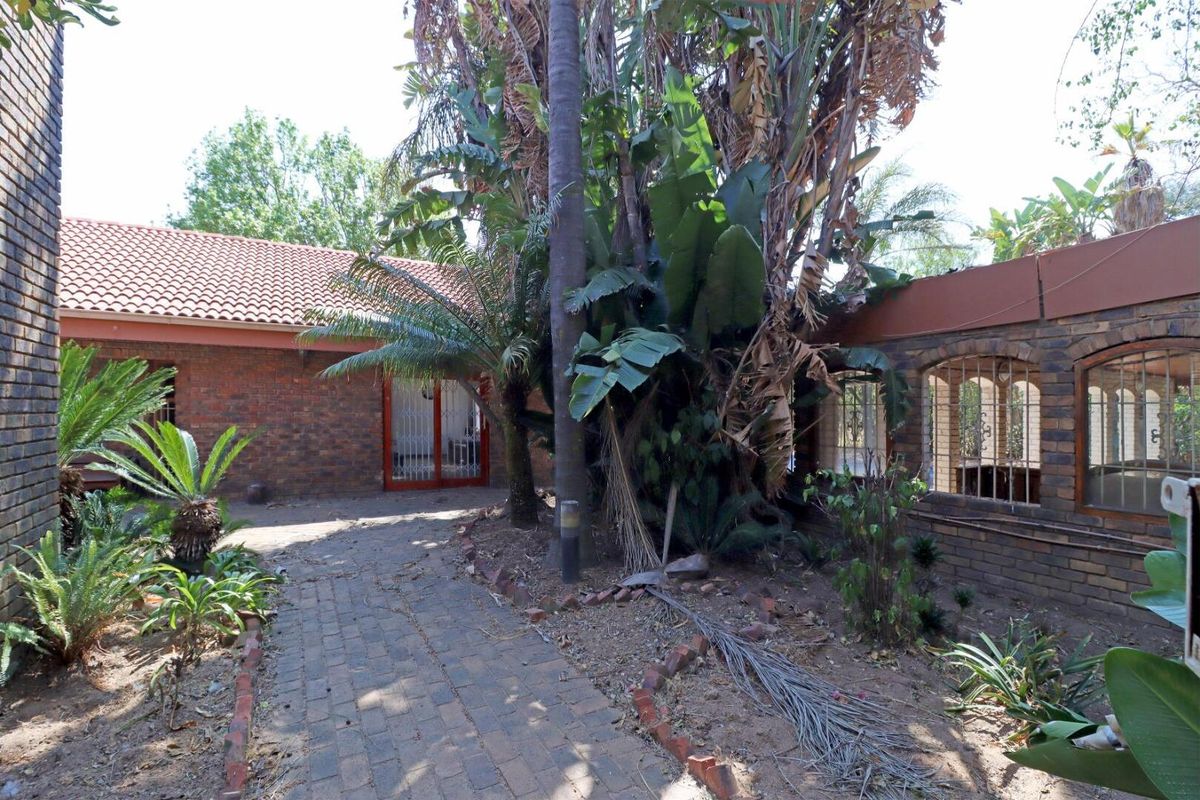 Rear exterior view of the property featuring a brick-paved pathway, brick walls, and established garden area with mature trees and security-fitted doors.