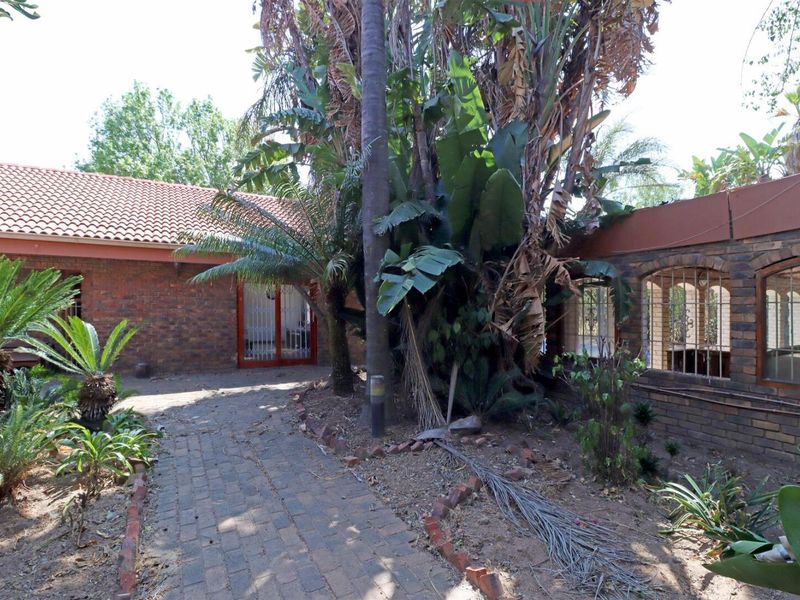 Rear exterior view of the property featuring a brick-paved pathway, brick walls, and established garden area with mature trees and security-fitted doors.