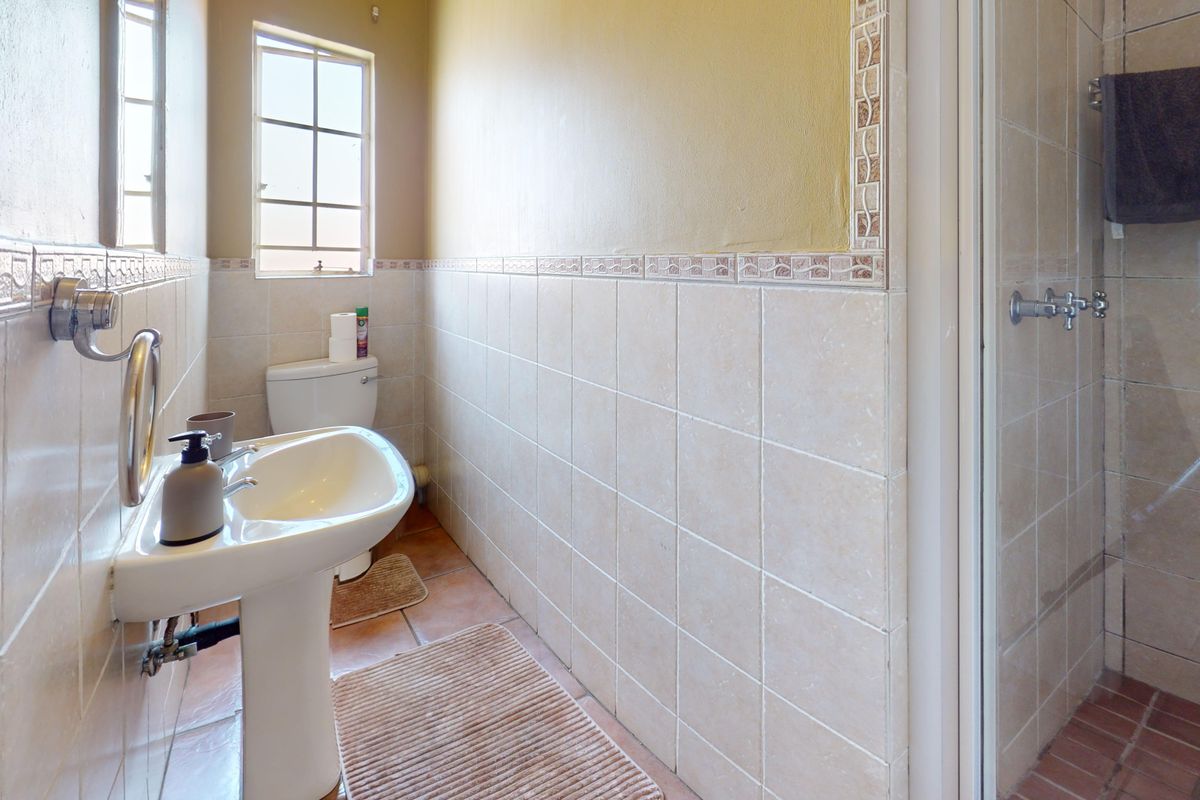 A functional bathroom featuring a pedestal sink, toilet, and a separate shower enclosure with neutral ceramic tiling throughout.