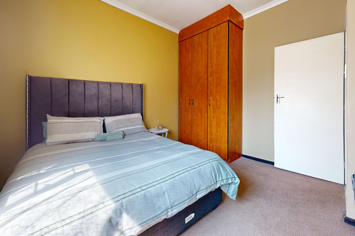A bedroom featuring mustard-toned walls, carpeted flooring, and a tall, wood-finish built-in wardrobe.