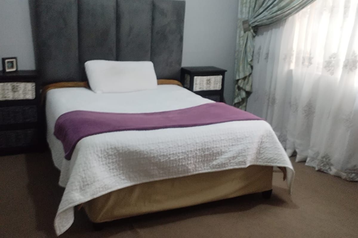 A well-maintained bedroom featuring neutral wall finishes, carpeted flooring, and a large window dressed with curtains.