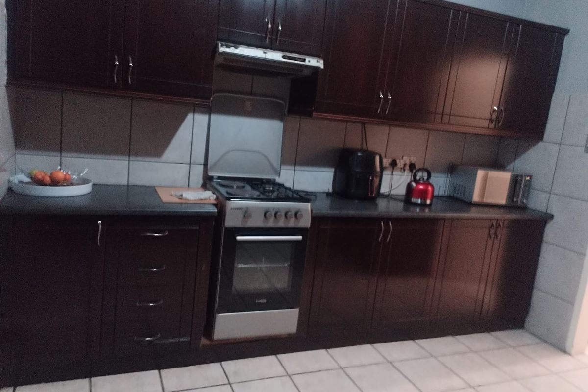 A functional kitchen featuring dark wood cabinetry, a built-in oven with extractor fan, and tiled flooring.