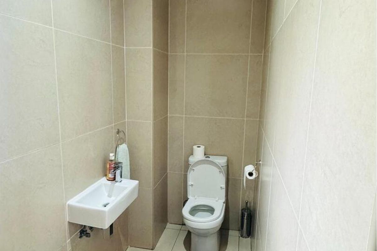 A compact guest bathroom featuring floor-to-ceiling neutral tiling, a wall-mounted basin, and a modern toilet suite.