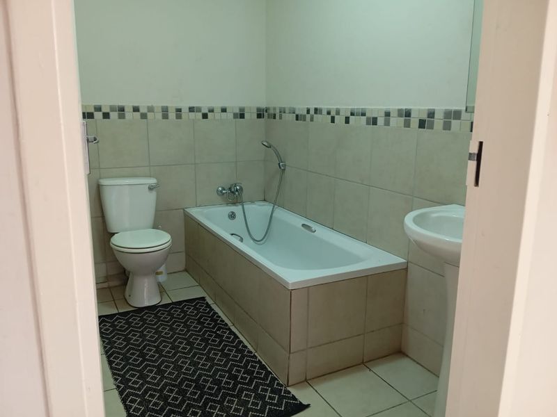 A functional bathroom featuring a bathtub, pedestal basin, and toilet with neutral wall and floor tiling.