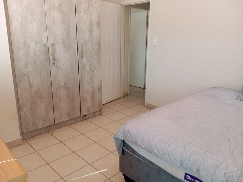 A bedroom featuring tiled flooring and built-in cupboards with a modern wood-look finish, providing functional storage space.