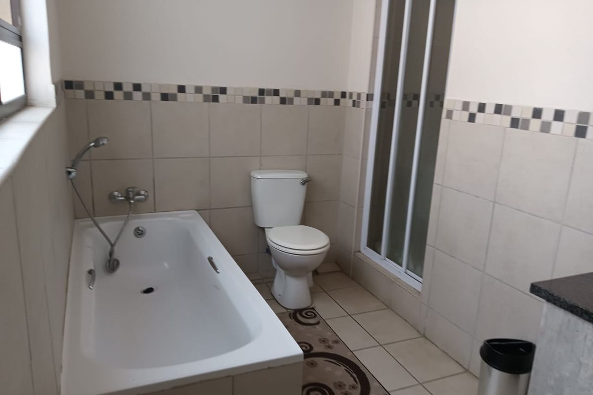 A functional bathroom featuring a built-in bathtub, a separate shower enclosure, and a toilet, finished with neutral wall and floor tiles.