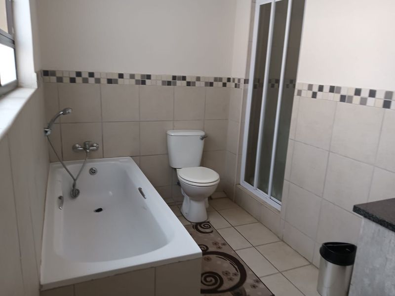 A functional bathroom featuring a built-in bathtub, a separate shower enclosure, and a toilet, finished with neutral wall and floor tiles.
