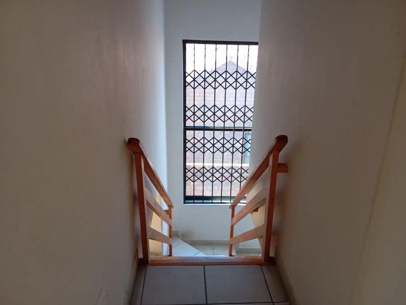 A functional hallway featuring a wooden staircase railing, tiled flooring, and a window secured with a metal security gate.
