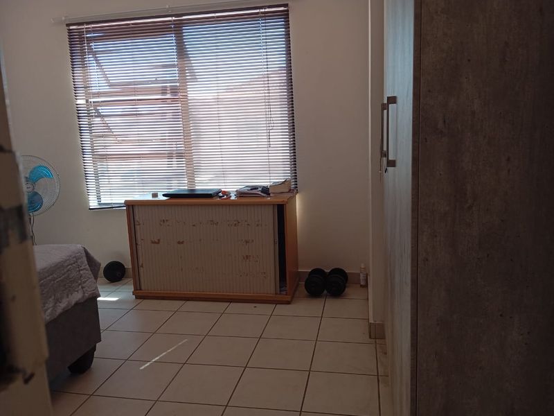 A bedroom featuring tiled flooring, a built-in wardrobe, and a window fitted with venetian blinds.