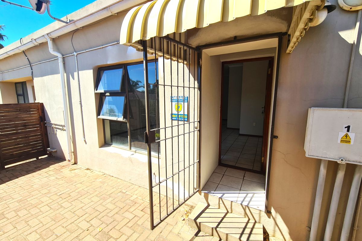 Rear exterior view of the townhouse featuring a paved patio area, security gate, and fixed awning over the entrance.