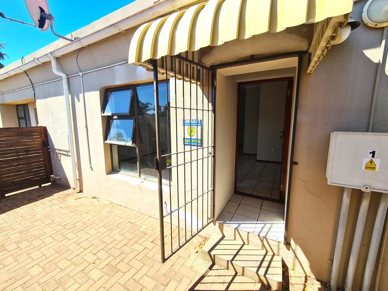 Rear exterior view of the townhouse featuring a paved patio area, security gate, and fixed awning over the entrance.