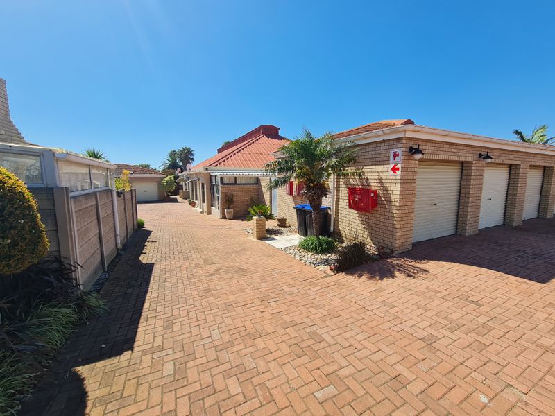A view of the townhouse complex driveway featuring face brick facades, multiple roller shutter garage doors, and neat brick paving.