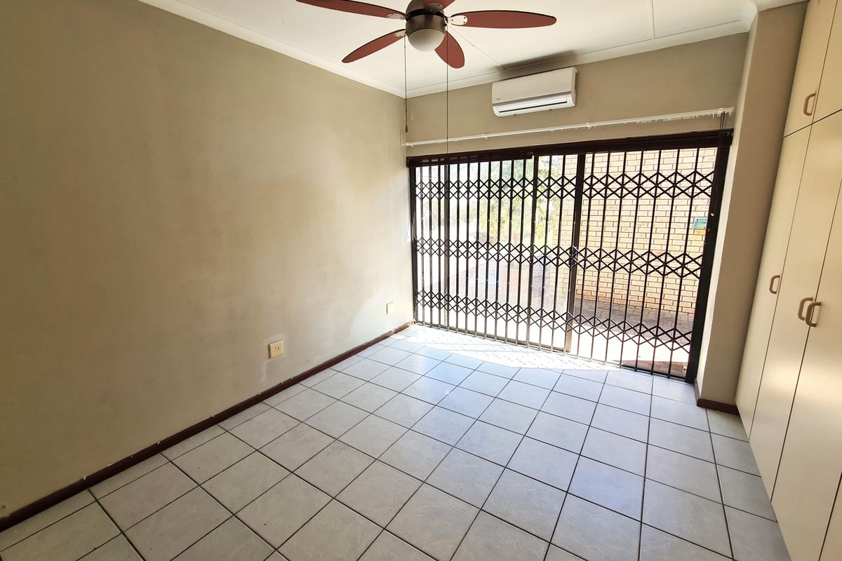 An empty bedroom featuring tiled flooring, built-in cupboards, a ceiling fan, and a split-system air conditioner with access to an outdoor area via security gate.