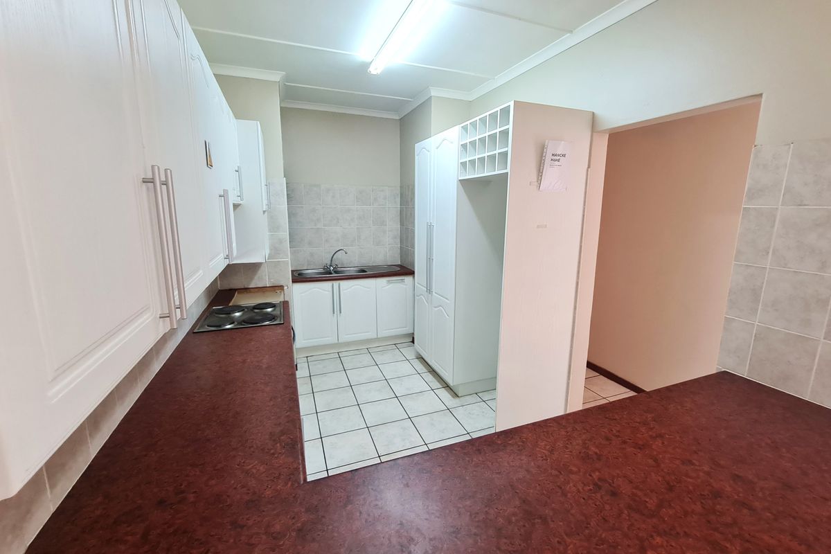 A functional kitchen featuring white cabinetry, dark laminate countertops, a built-in electric hob, and tiled flooring, offering a clean and practical workspace.