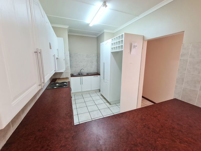 A functional kitchen featuring white cabinetry, dark laminate countertops, a built-in electric hob, and tiled flooring, offering a clean and practical workspace.
