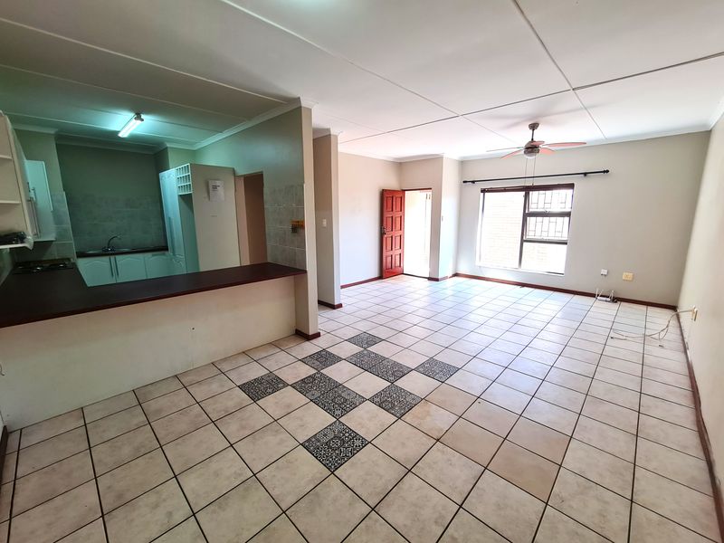 Spacious open-plan living and kitchen area featuring tiled flooring, a breakfast bar, and direct access to the exterior through a secure door.