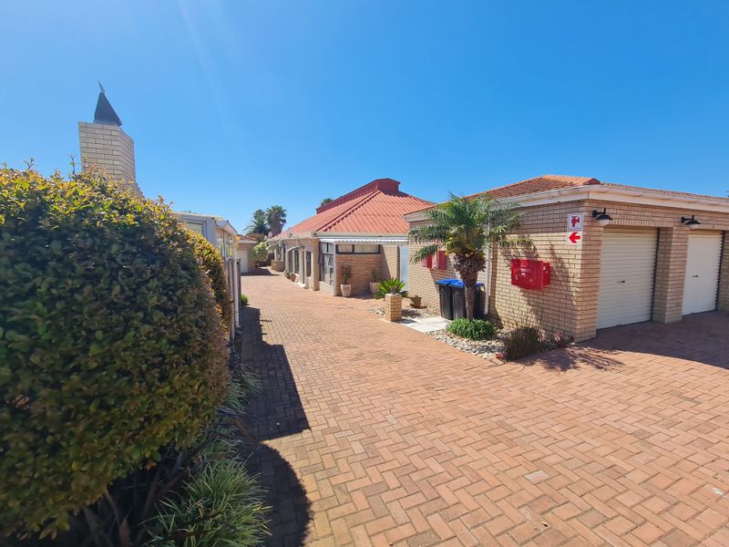 A view of the townhouse complex driveway featuring facebrick facades, double garages with roll-up doors, and neat brick paving.