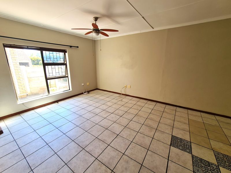 An empty living room featuring tiled flooring, a ceiling fan, and large windows with security bars, offering a blank canvas for interior design.