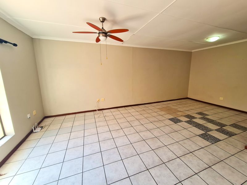 An empty living room featuring tiled flooring, a ceiling fan, and neutral wall tones, offering a blank canvas for personalization.