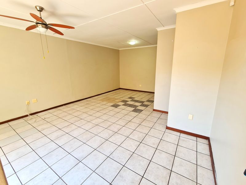 An empty, open-plan living area featuring neutral wall tones, tiled flooring, and a ceiling fan, offering a blank canvas for personalization.
