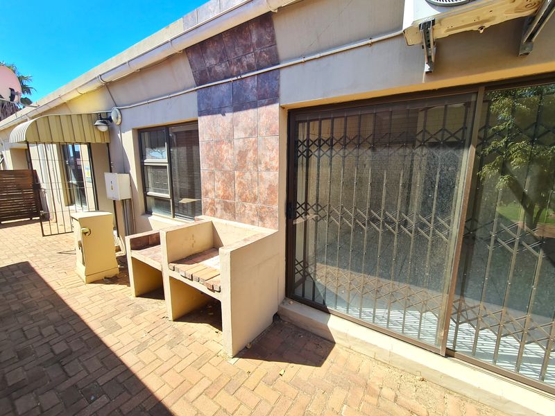 Outdoor patio area featuring a built-in braai, paved flooring, and a sliding glass door with security gate access to the interior.