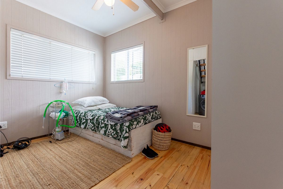 A bedroom featuring timber flooring, neutral wall paneling, and natural light through venetian blinds.