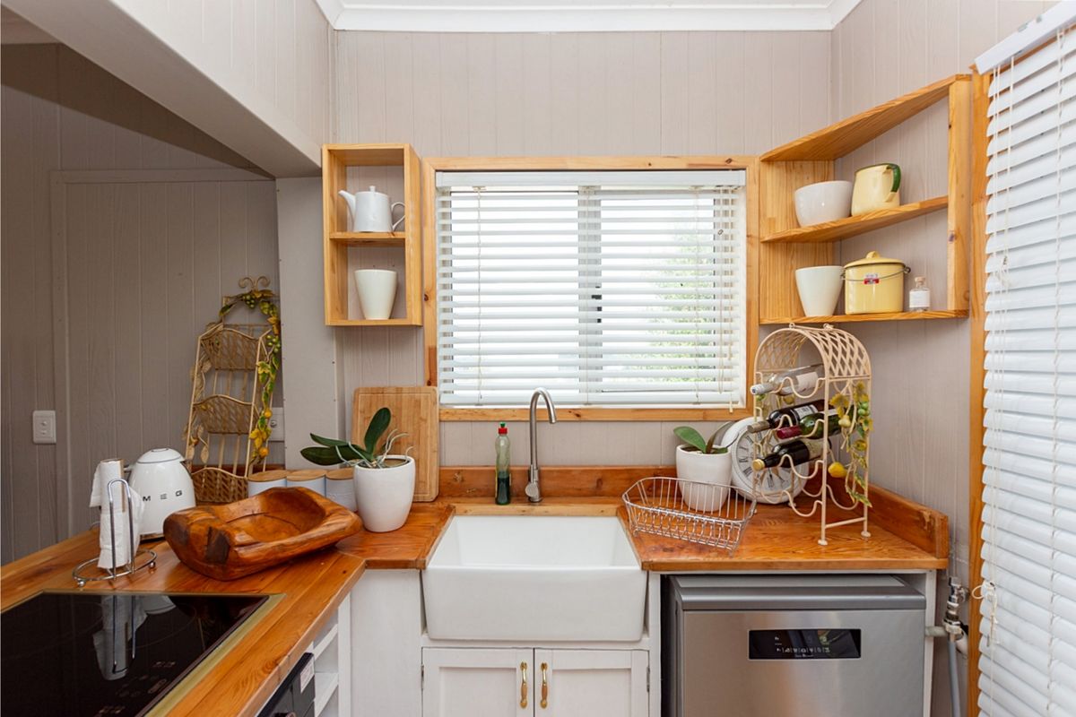 A compact kitchen featuring a farmhouse sink, timber countertops, open shelving, and integrated appliances, offering a cozy and functional workspace.