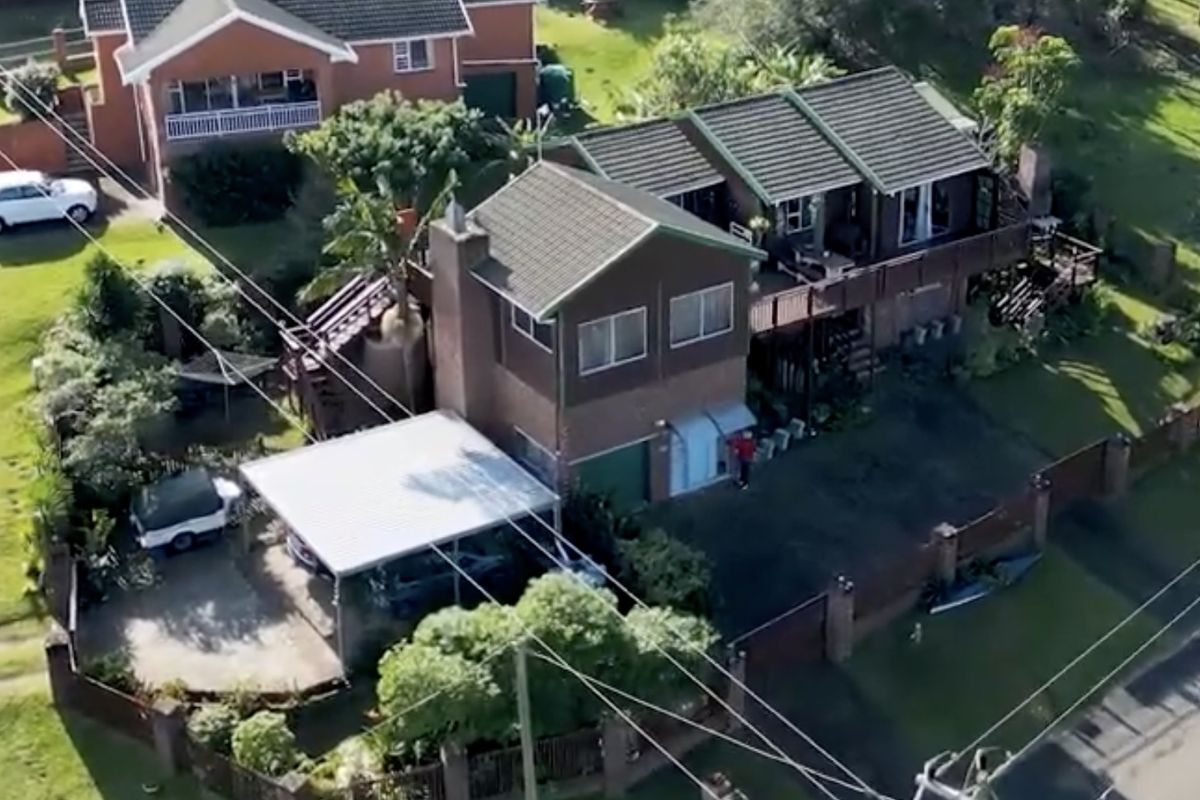 Aerial view of a multi-level residential property featuring a tiled roof, brick exterior, timber decking, and a detached carport.