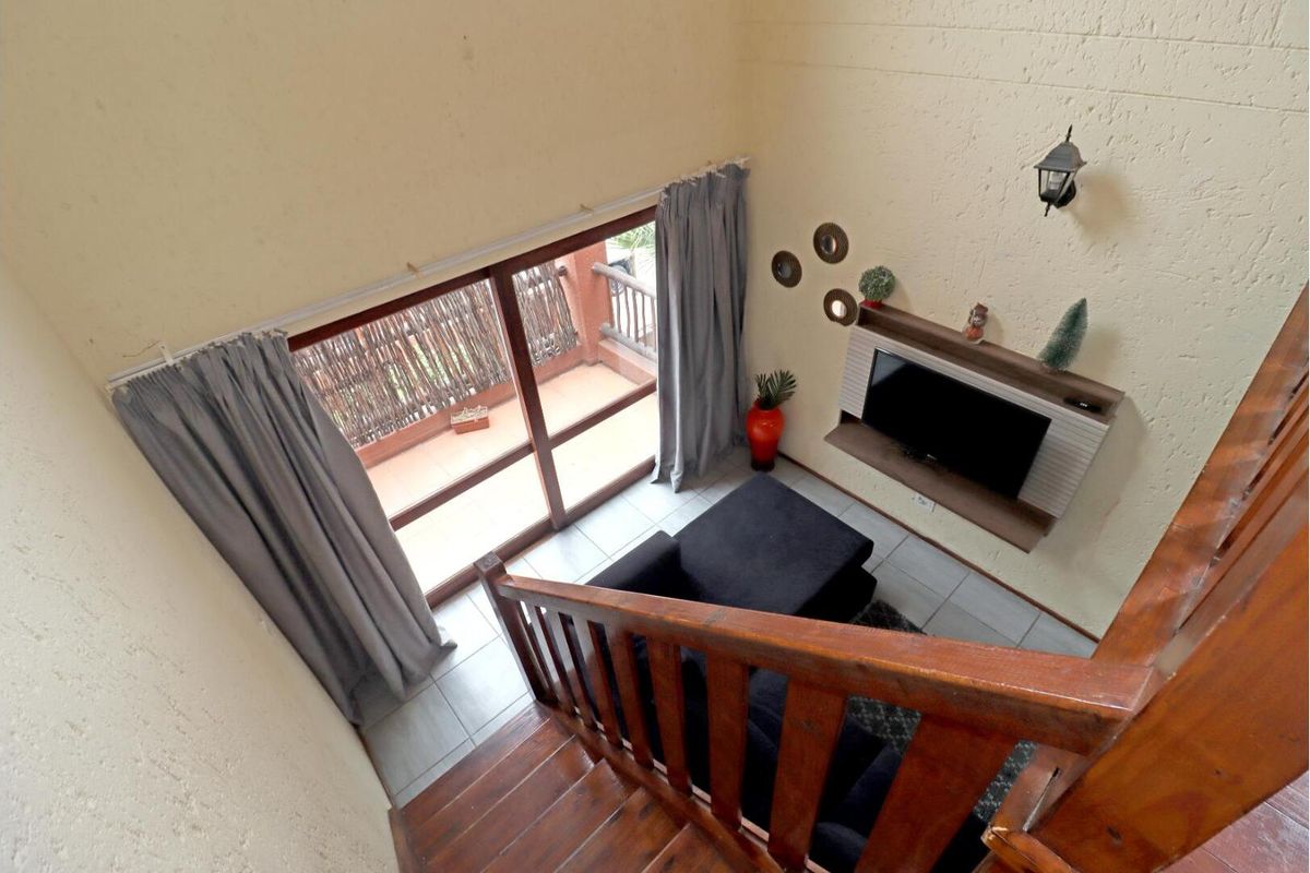 A high-angle view of a living area featuring a wooden staircase, tiled flooring, and sliding glass doors leading to a balcony.
