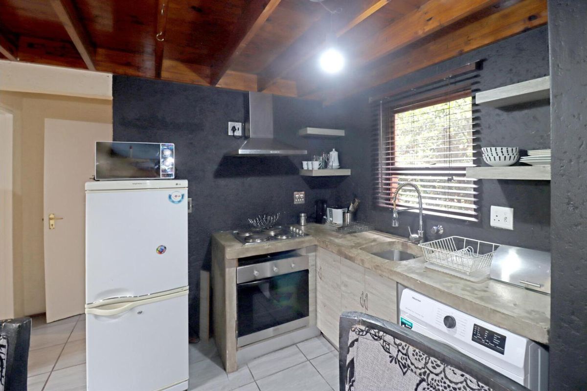 Compact kitchen featuring concrete-style countertops, built-in oven, gas hob, extractor fan, and exposed timber ceiling beams.
