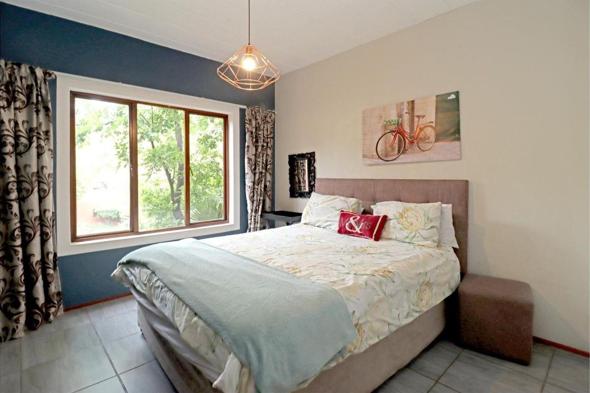 A bedroom featuring tiled flooring, a large window with garden views, and a feature wall, providing a comfortable and well-lit living space.