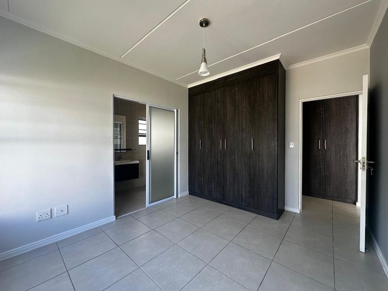 A spacious, well-maintained bedroom featuring neutral tiled flooring, ample built-in dark wood cupboards, and direct access to an en-suite bathroom.