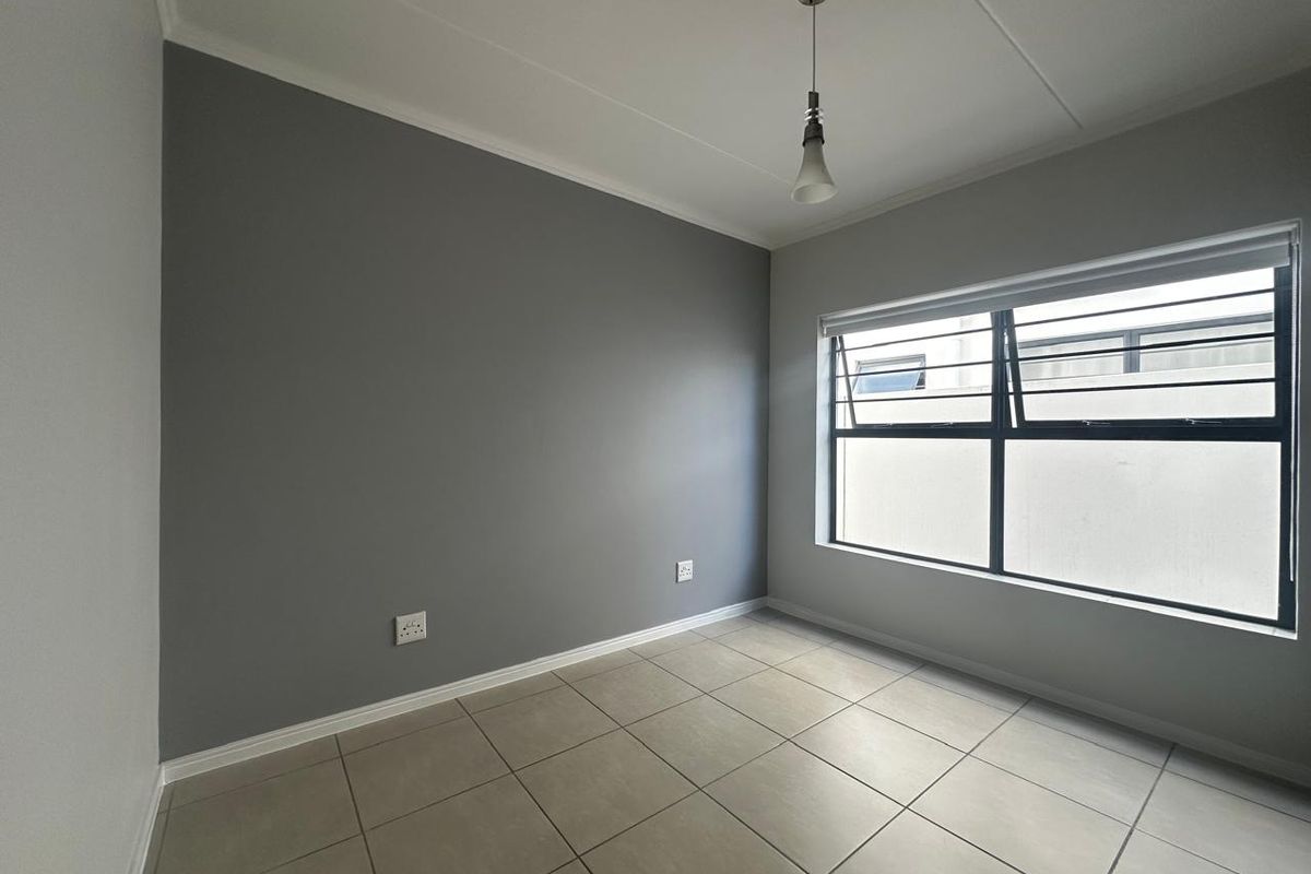 A clean, empty bedroom featuring neutral grey accent walls, tiled flooring, and a window fitted with security bars.
