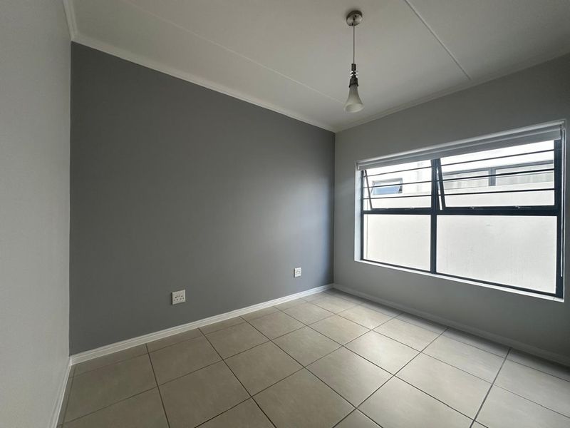 A clean, empty bedroom featuring neutral grey accent walls, tiled flooring, and a window fitted with security bars.