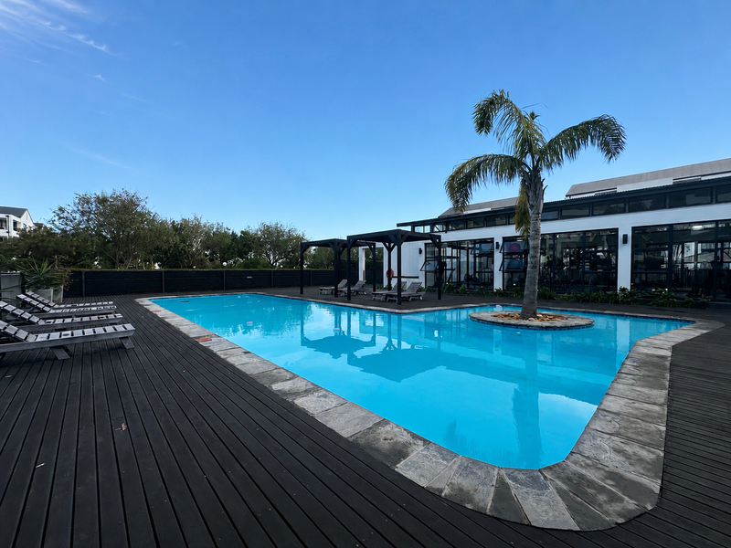 A well-maintained outdoor swimming pool area featuring timber decking, stone coping, and a central palm tree, complemented by a modern pergola structure.