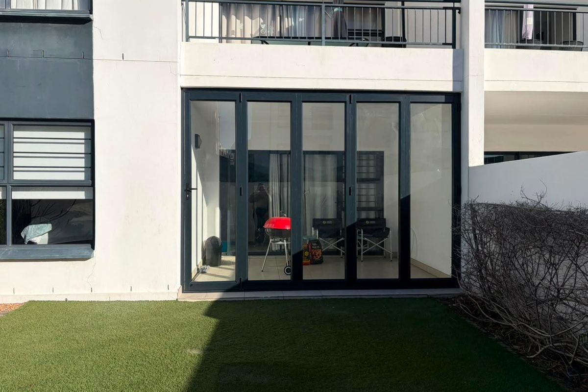 Rear view of the apartment featuring a ground floor patio with modern folding glass doors and an upper level balcony with metal railings.