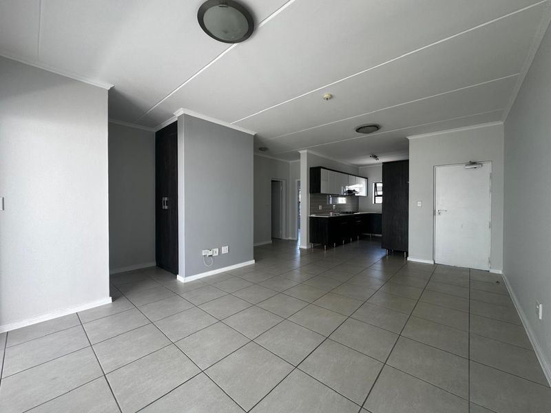 Spacious open-plan living area featuring neutral tiled flooring, clean wall finishes, and a modern kitchen with built-in cabinetry and integrated appliances.