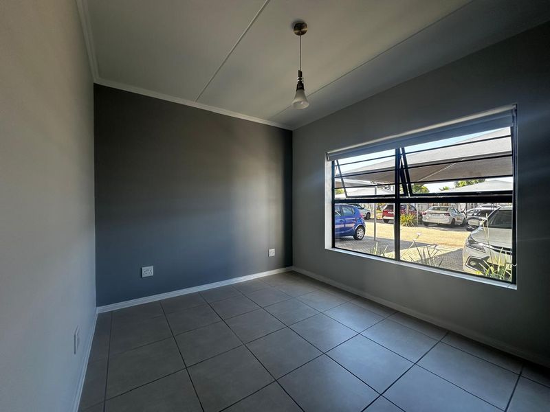 A bright, empty bedroom featuring neutral grey walls, large window with natural light, and modern tiled flooring, ready for personalization.