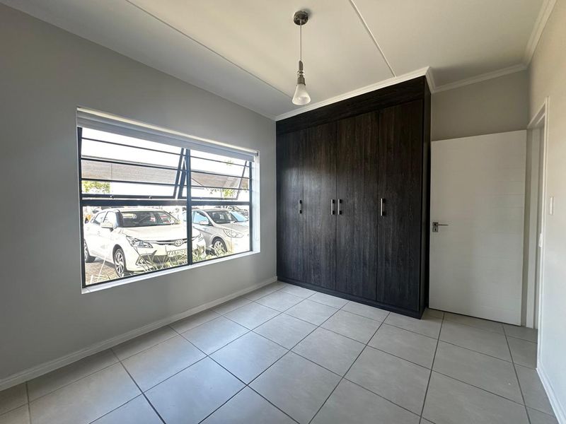 A bright, empty bedroom featuring neutral tiled flooring, a large window, and dark wood-finish built-in cupboards.