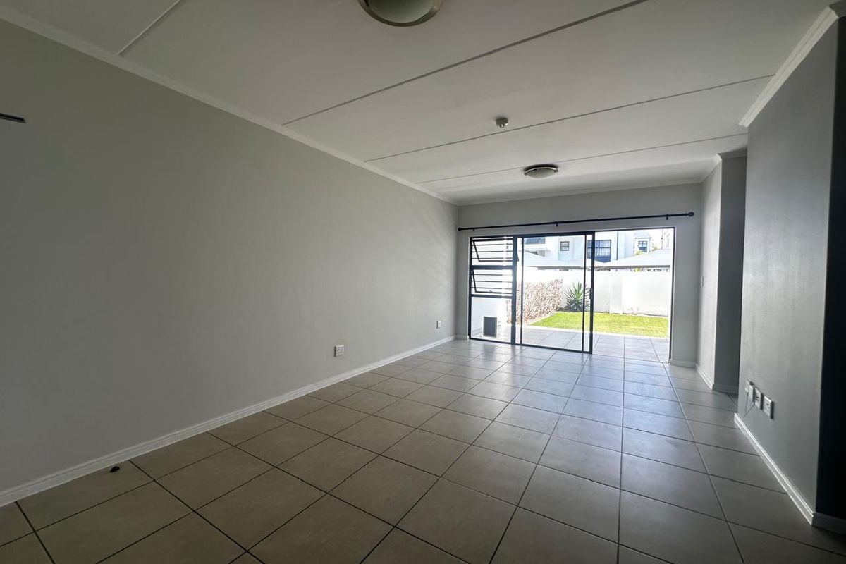 An empty, open-plan living area featuring neutral tiled flooring and a large sliding glass door providing direct access to the rear garden.