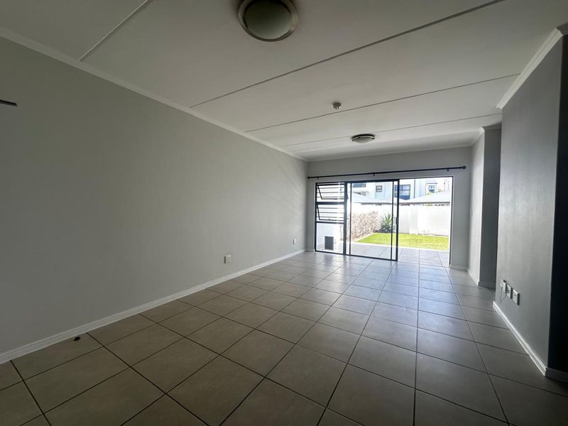 An empty, open-plan living area featuring neutral tiled flooring and a large sliding glass door providing direct access to the rear garden.