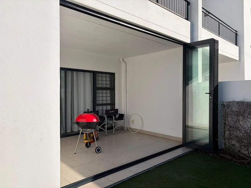 A covered patio area featuring tiled flooring and modern bi-fold glass doors that open onto a small garden space.