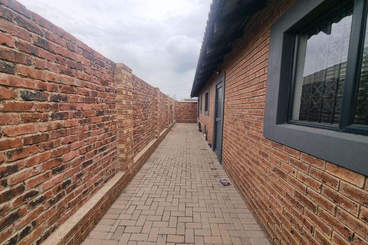 A narrow side passage featuring paved flooring, exposed brick boundary wall, and exterior access to the main dwelling structure.
