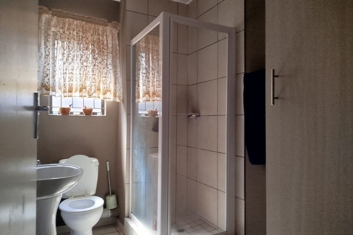 A functional bathroom featuring a pedestal basin, toilet, and a glass-enclosed shower with tiled finishes and built-in storage.