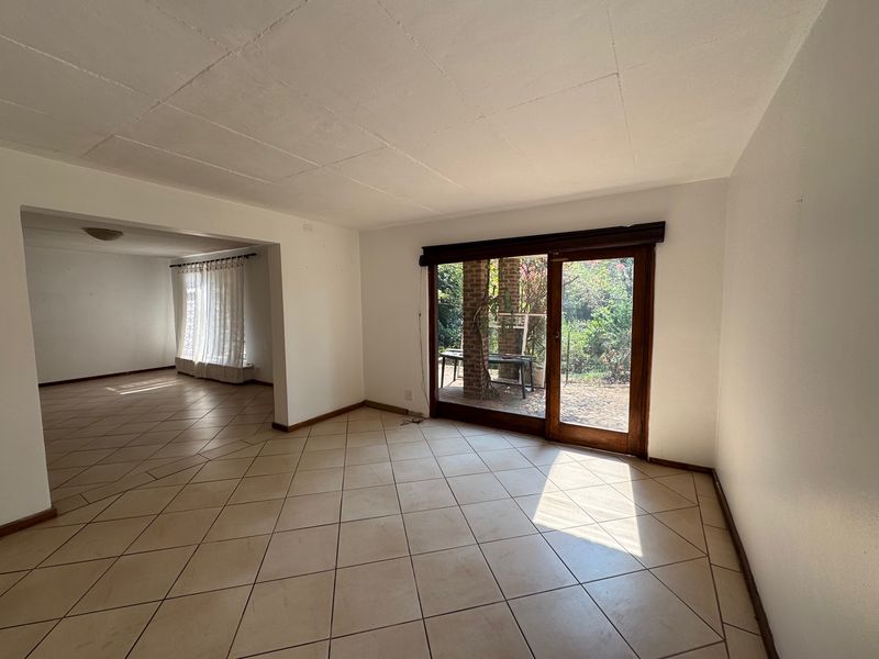 An empty, open-plan living area featuring tiled flooring and a sliding glass door providing access to the rear garden.