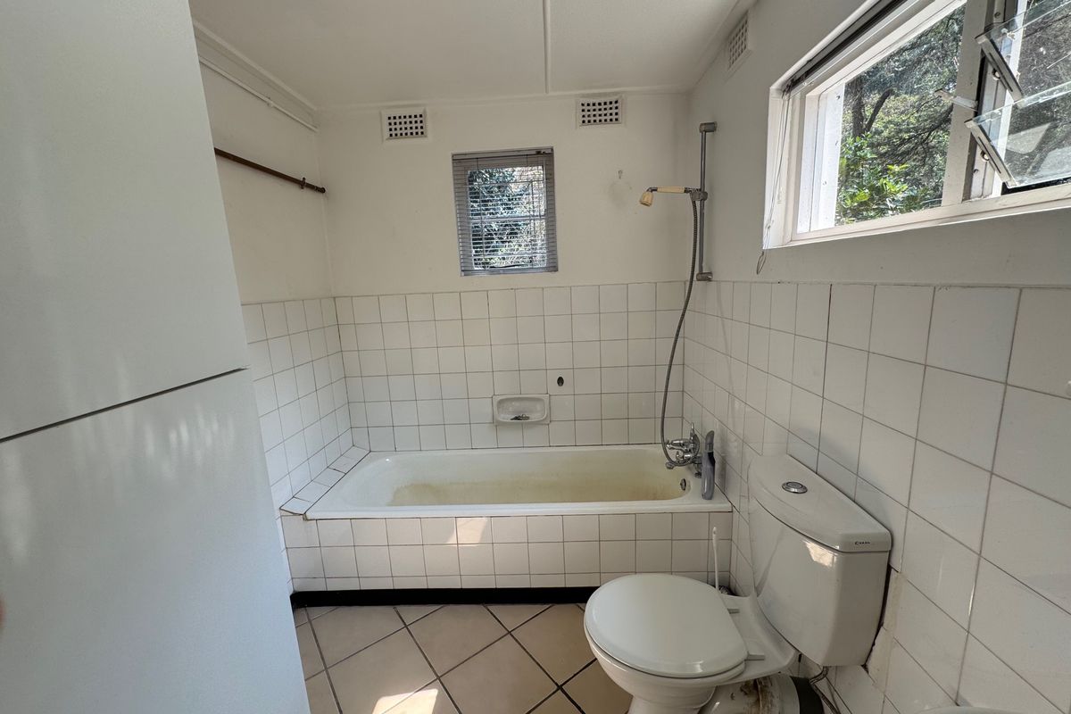 A dated bathroom featuring a built-in bathtub, ceramic tiling, and standard fixtures, requiring cosmetic updates to modernize the space.